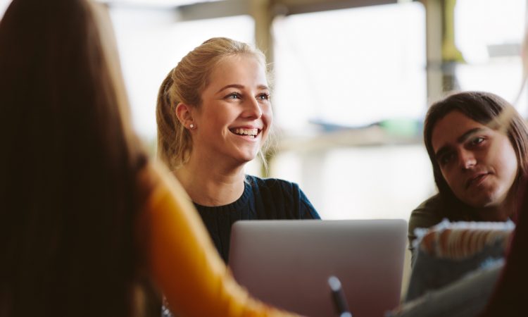 Female student sitting amongst classmates and smiling in lecture room.