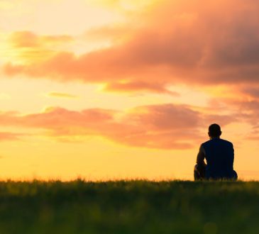 man sitting in field watching sunset