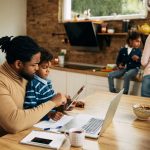 man sitting at kitchen table working with son in lap