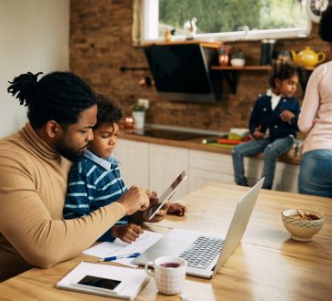 man sitting at kitchen table working with son in lap