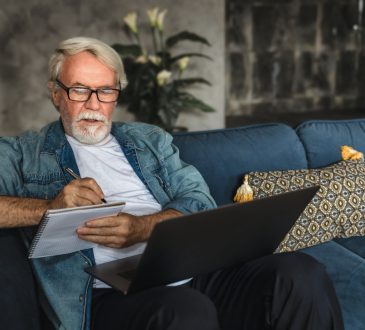 older man writing notes in notebook watching webinar