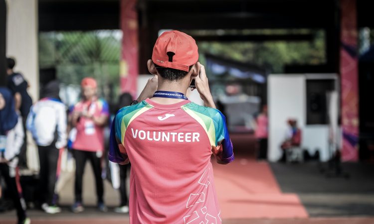 man wearing shirt with "volunteer" on the back taking photo at outdoor event