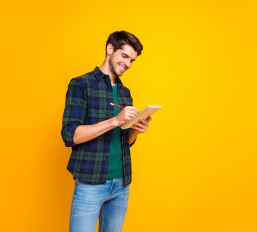 man standing and writing in notebook against bright yellow background