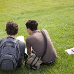two male students with homework sitting on grass