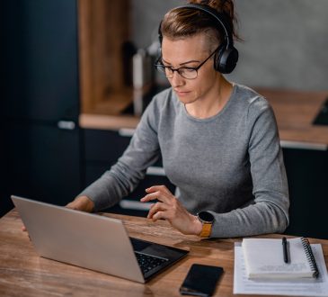 Focused woman wearing headphones, watching a webinar and writing notes.