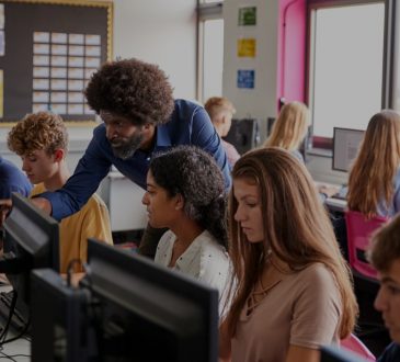 male teacher helping high school students in computer lab