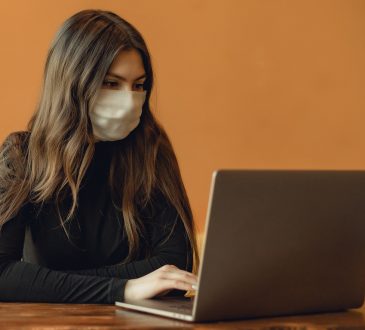 woman wearing mask typing on laptop