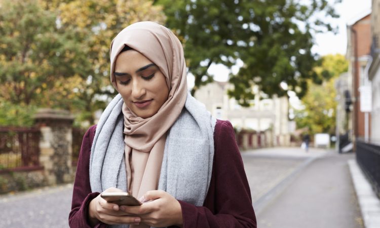 woman wearing hijab walking outside and texting