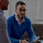 man sitting on couch in office talking to colleagues