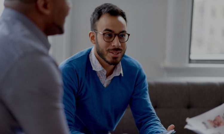 man sitting on couch in office talking to colleagues