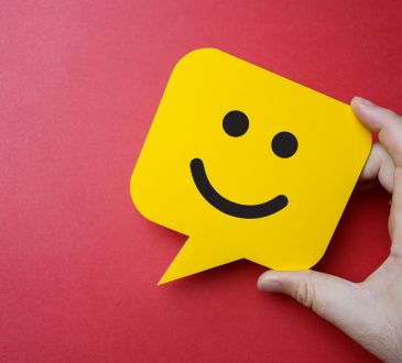 Man holding yellow speech bubble with smiley face on red background.