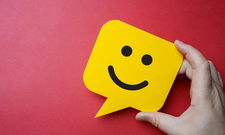 Man holding yellow speech bubble with smiley face on red background.
