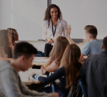 Female teacher smiling at students at front of high school classroom.