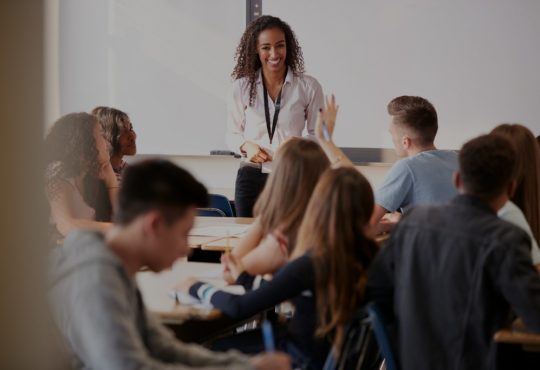 Female teacher smiling at students at front of high school classroom.