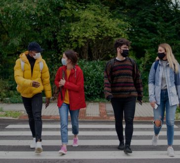 Four college students walking across crosswalk wearing masks.