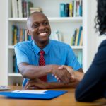 Man in bright blue button-up shirt shaking hands with woman in job interview