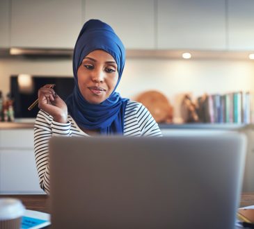 Woman wearing hijab working at kitchen table.
