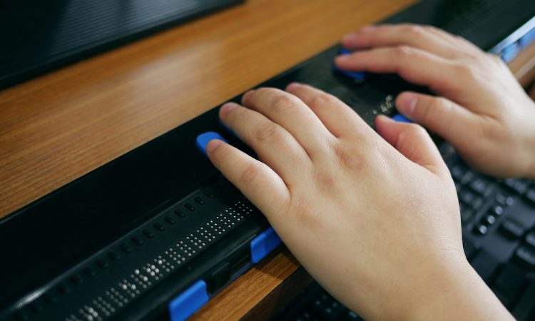 Close-up of hands using computer with braille display.