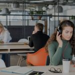 Young woman wearing headphones in open-concept office.