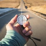 Compass in hand in front of mountain road background.
