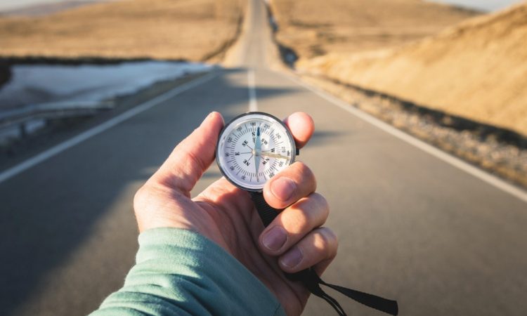Compass in hand in front of mountain road background.