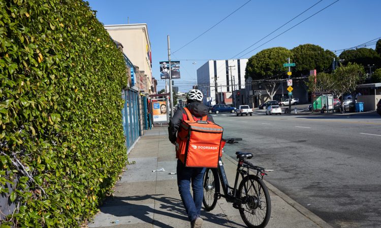A DoorDash delivery worker walks his bike along the road.