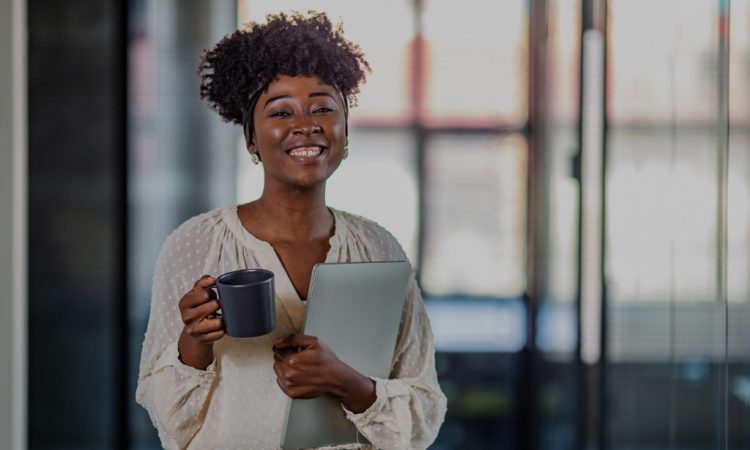 Young woman standing in office holding laptop and smiling.