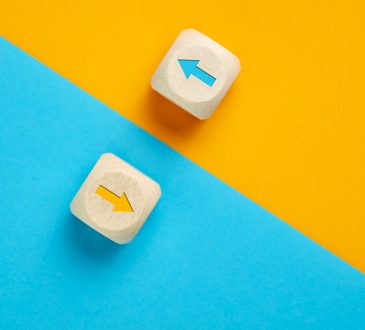 Arrow icons in contrast on wooden cubes moving towards opposite directions.