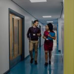 Man and woman walking down school hallway talking.