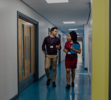 Man and woman walking down school hallway talking.