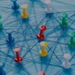 An arrangement of colorful pins linked together with string on a pale blue background.