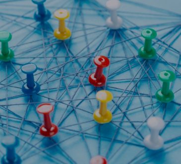 An arrangement of colorful pins linked together with string on a pale blue background.