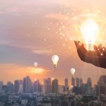 Hand holding light bulb on city background