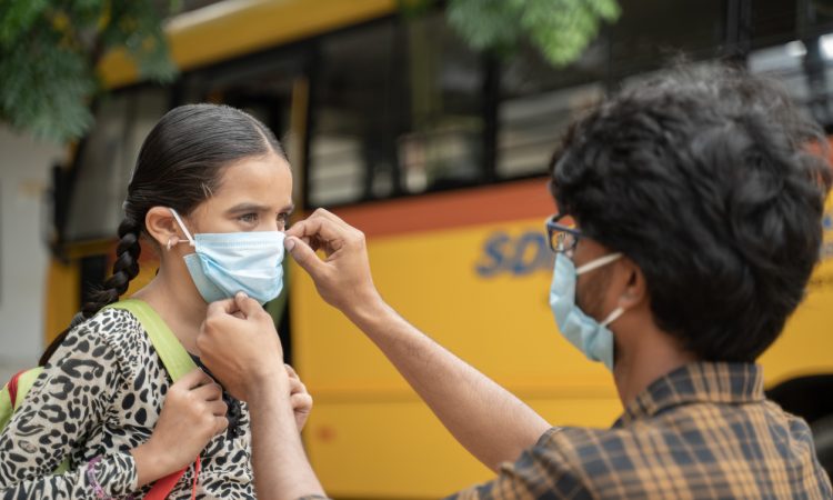 Father helping daughter to wear mask before getting on school bus