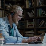 Man smiling and working on laptop with bookshelves in background