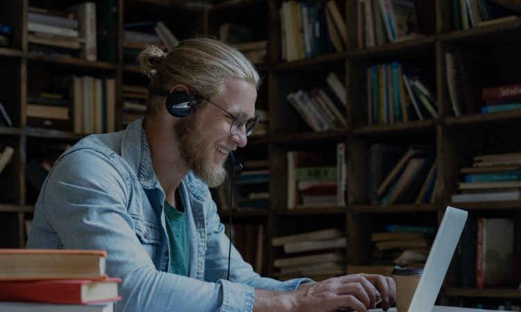 Man smiling and working on laptop with bookshelves in background