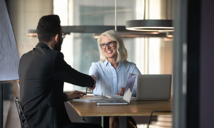 Smiling mature businesswoman shaking hand of young businessman