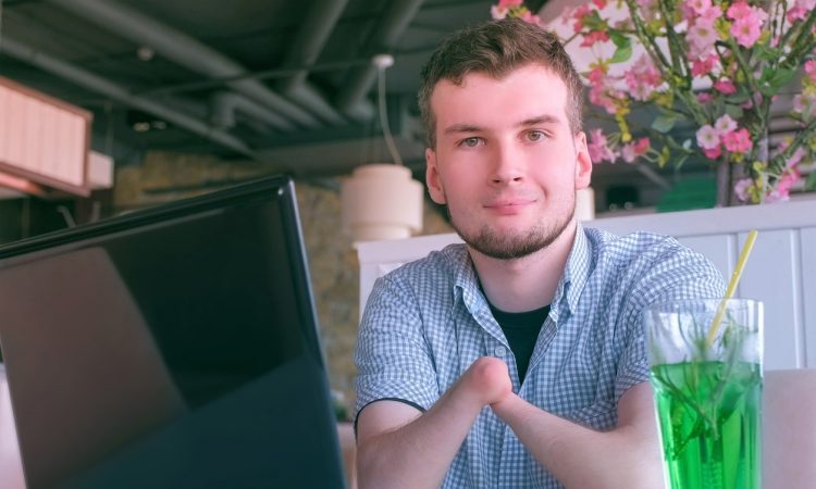 Young man with no hands sitting at laptop in cafe