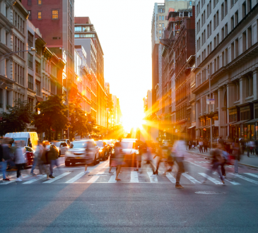 Sun setting behind pedestrians on downtown city street.