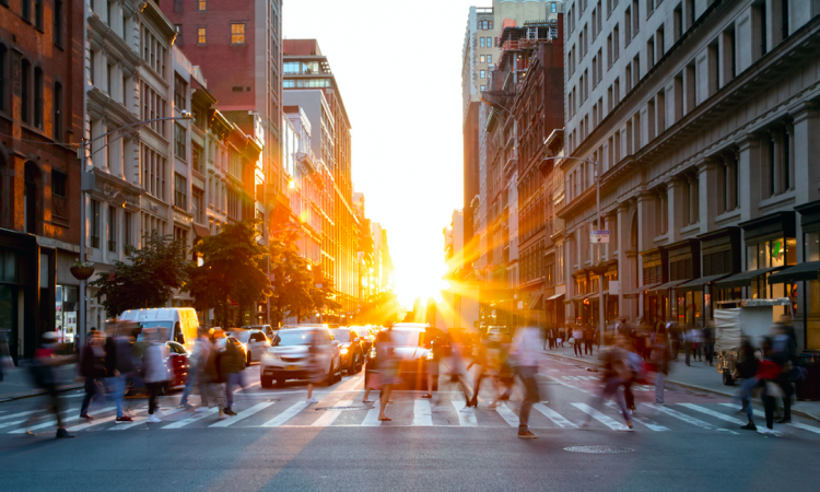 Sun setting behind pedestrians on downtown city street.