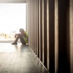 Man wearing hard hat and safety vest sitting with head hanging in container box at shipyard