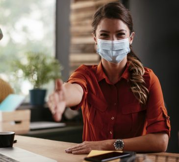 Woman wearing mask reaching hand out for handshake in office