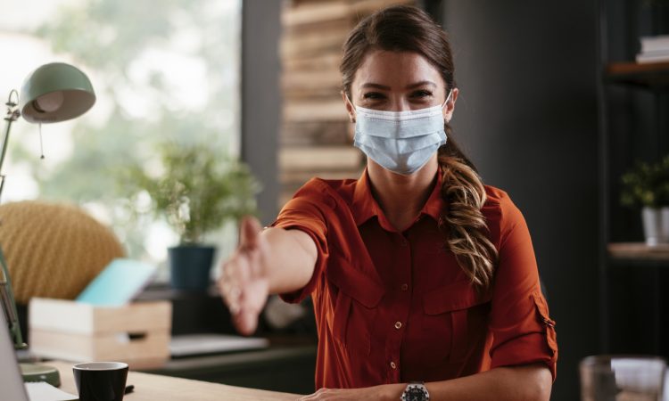 Woman wearing mask reaching hand out for handshake in office