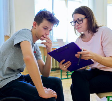 Adult sitting and talking to youth in classroom.