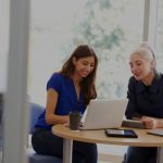 Two women sitting at table looking at laptop together
