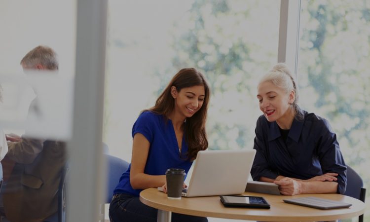 Two women sitting at table looking at laptop together