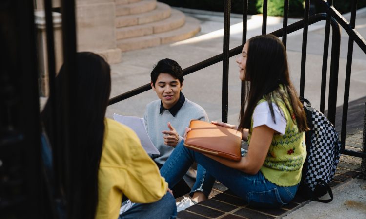 Three students sitting and talking on stairs outside.