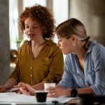 Two women looking at papers on desk together