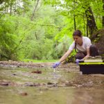 Woman taking sample of water from stream