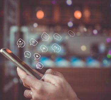 Hands typing on smartphone with chat bubbles above screen.